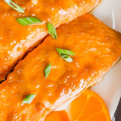 Horizontal image of orange ginger baked salmon filets next to a bowl of white rice.