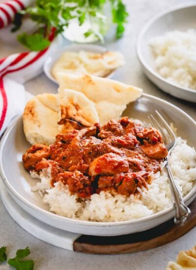Chicken tikka masala over a bed of rice in a shallow bowl with teared naan bread.