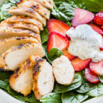 A bowl of strawberry spinach salad with grilled chicken and poppy seed dressing.