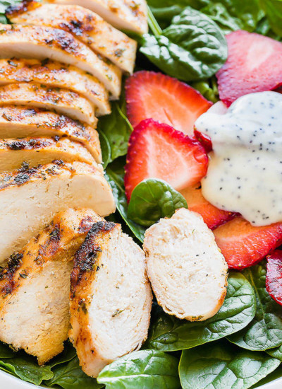 A bowl of strawberry spinach salad with grilled chicken and poppy seed dressing.