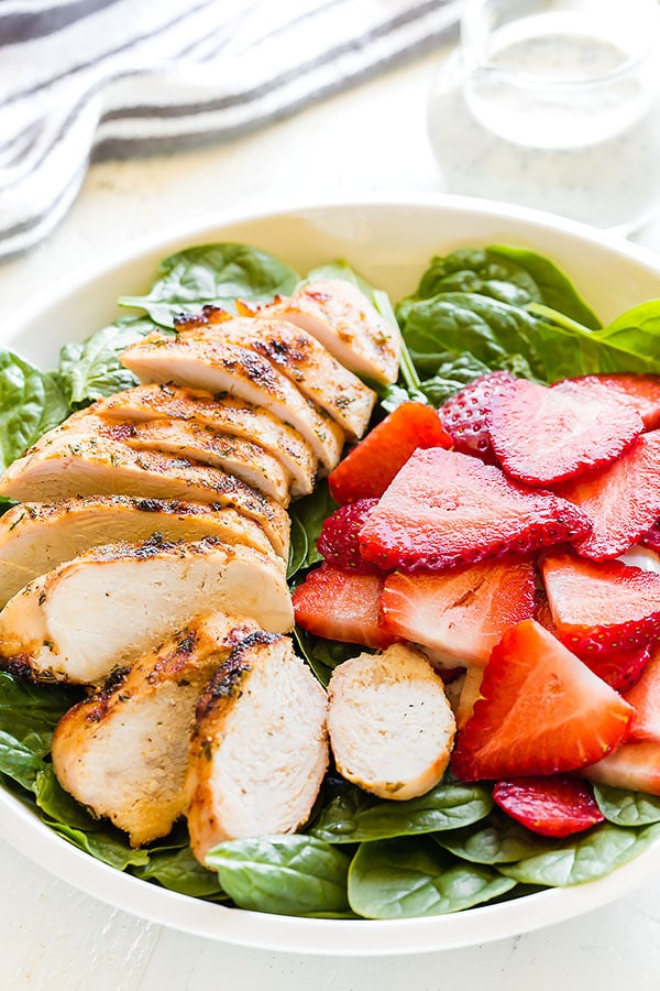 Spinach salad in a bowl topped with sliced strawberries and grilled chicken breast.