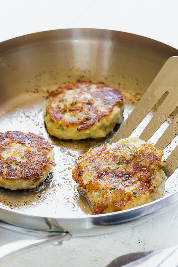 Loaded mashed potato patties in a skillet.