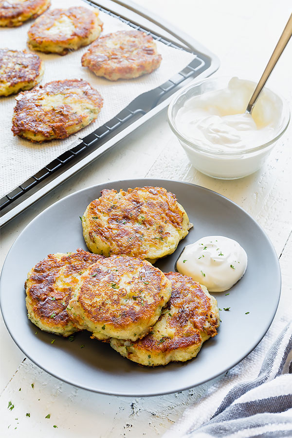 Mashed potato patties on a plate with a dollop of sour cream on the side.