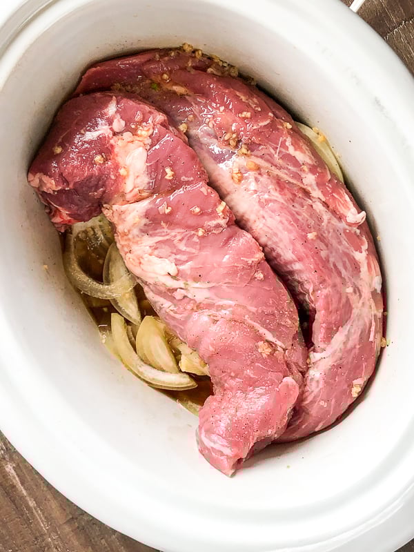 Onions and pork tenderloins in the bowl of a slow cooker.  