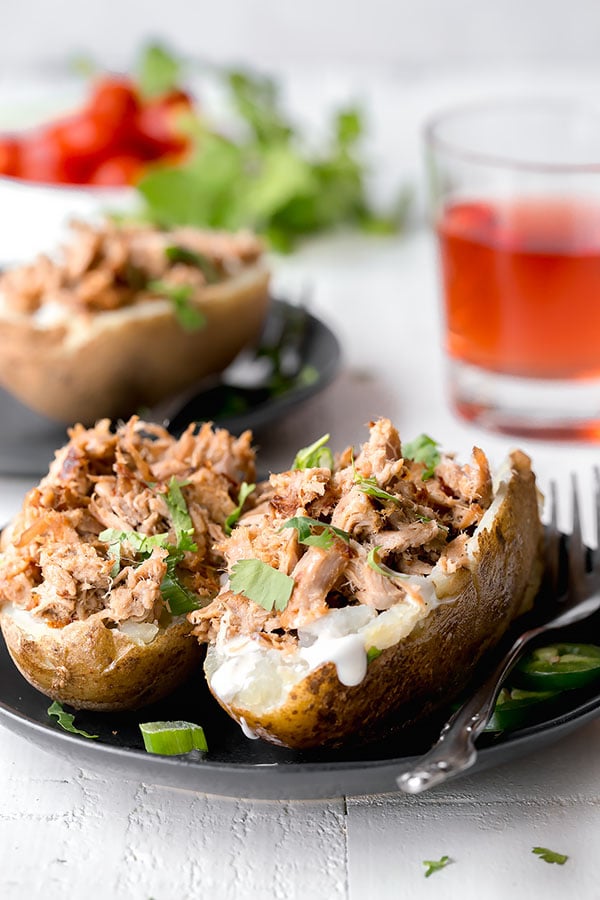 Slow cooker pork tenderloin shredded and stuffed in a baked potato on a plate. 