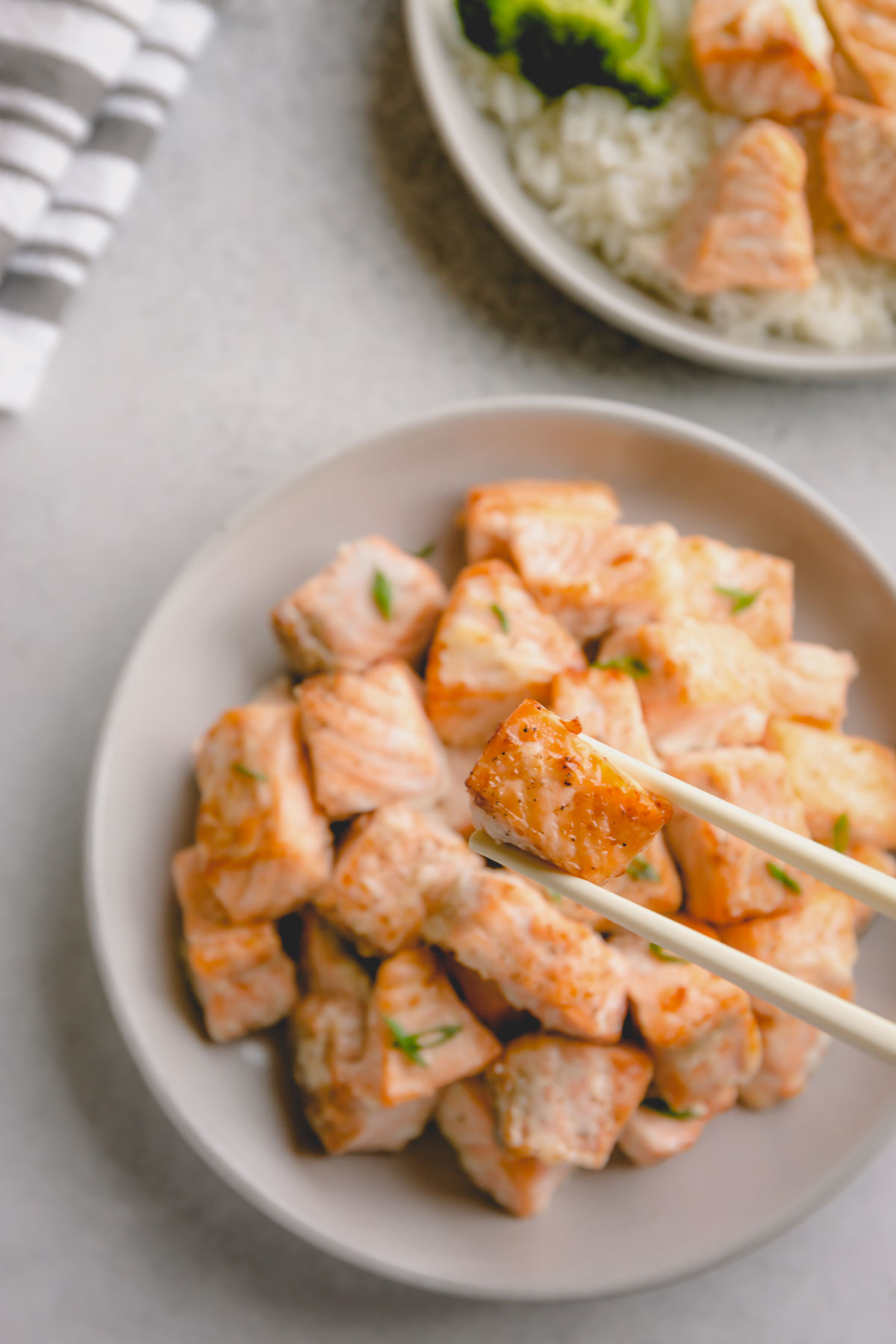 Baked salmon chunks on plate with one piece of salmon held with chopsticks.