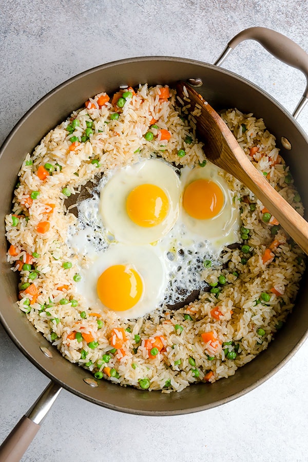 Three eggs in the center of a skillet of vegetable fried rice. 