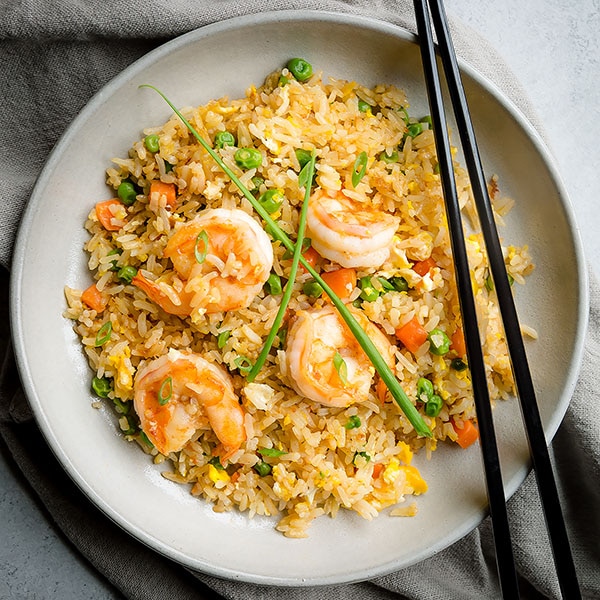 A bowl of shrimp fried rice with two chopsticks on top. 