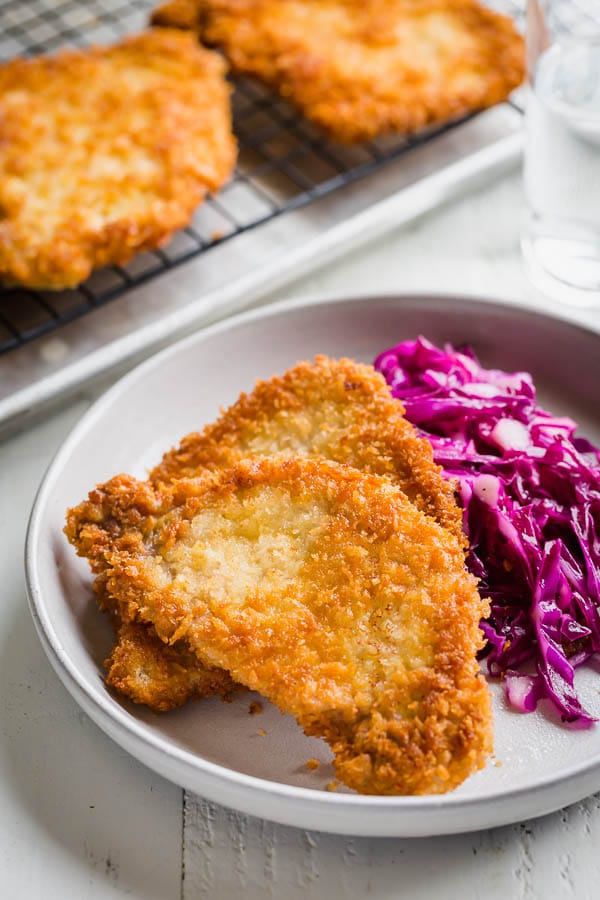 A bowl of breaded pork cutlets with red cabbage next to pork cutlets on a wire rack. 