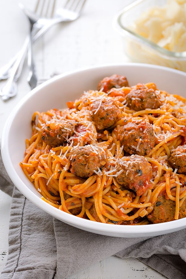A bowl of spaghetti and meatballs topped with parmesan cheese. 