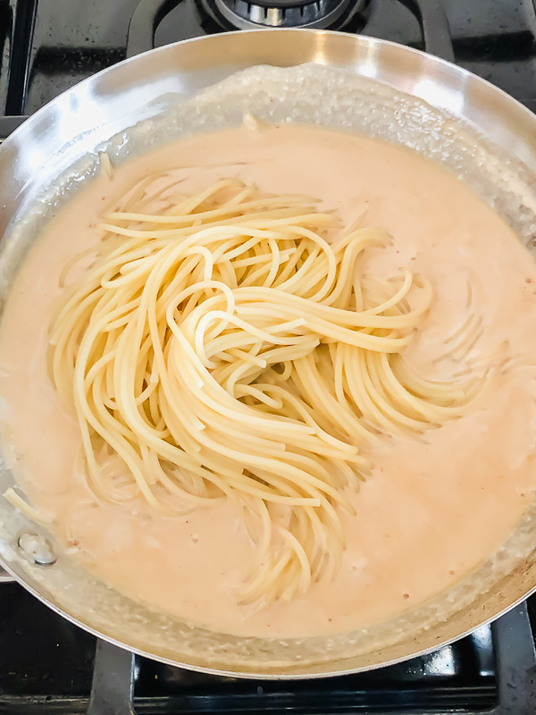 Spaghetti noodles being stirred into white wine sauce in a skillet. 