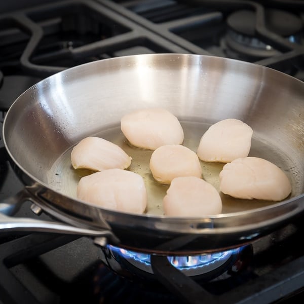 Raw scallops cooking in a pan with oil. 
