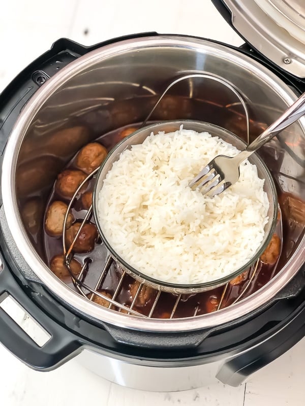 A bowl of cooked white rice and BBQ meatballs in an Instant pot with a fork sticking out of the rice. 