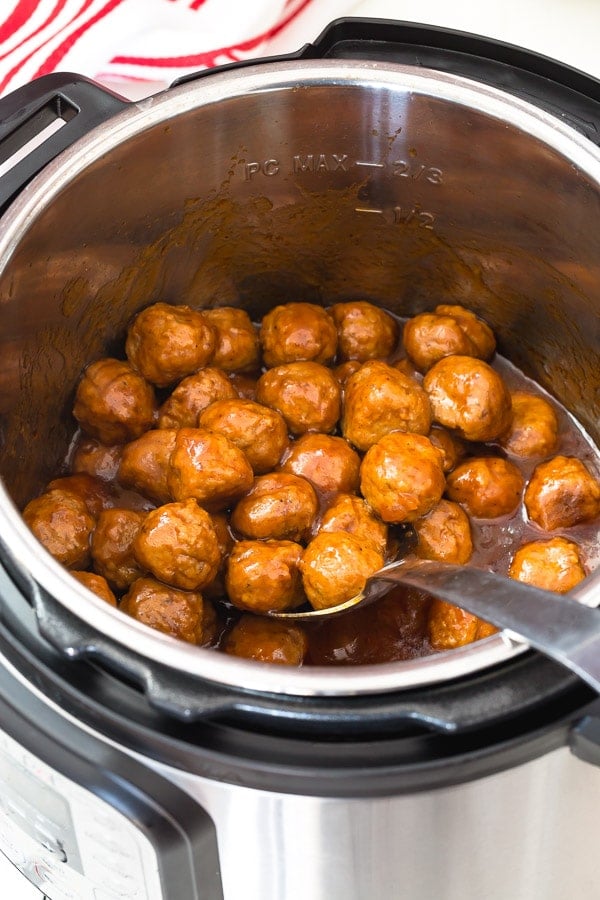 A spoon lifting a scoop of beer BBQ meatballs from an Instant Pot. 