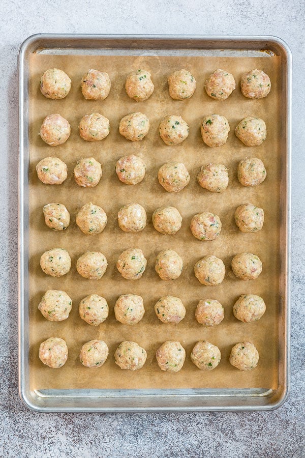 Unbaked bacon chicken meatballs on a parchment paper lined baking sheet. 