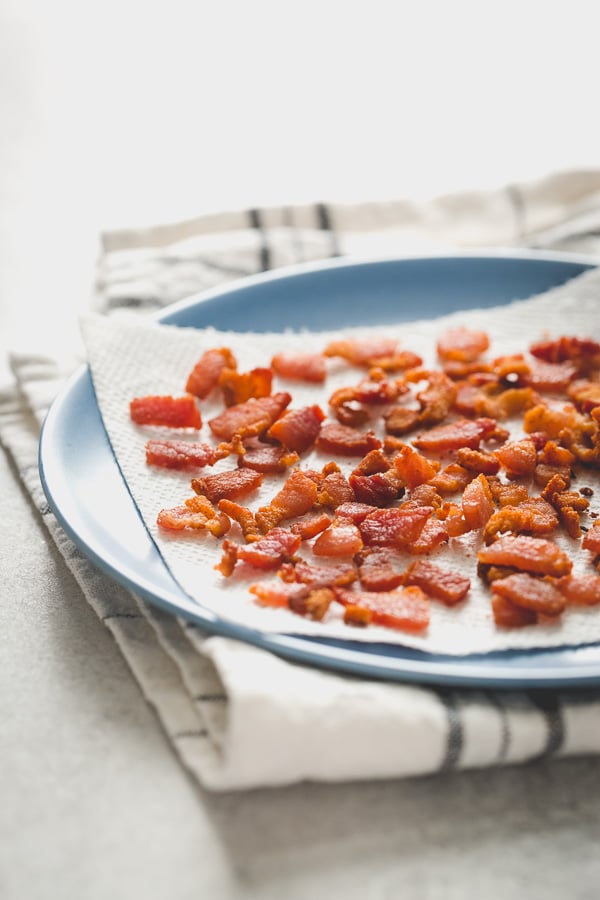 Crispy bacon pieces on top of a paper towel on a plate. 
