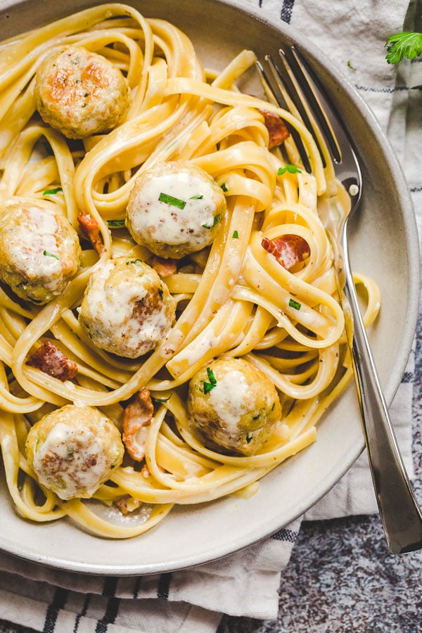 A plate of bacon chicken meatballs with bacon cream sauce and pasta. 