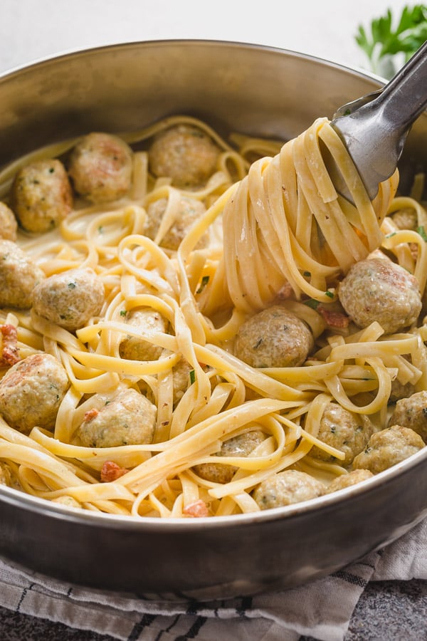 A skillet full of bacon chicken meatballs with linguini pasta. 