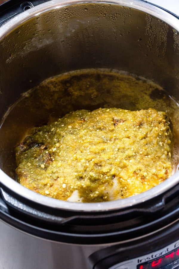A pork loin roast covered with salsa verde in an Instant Pot. 