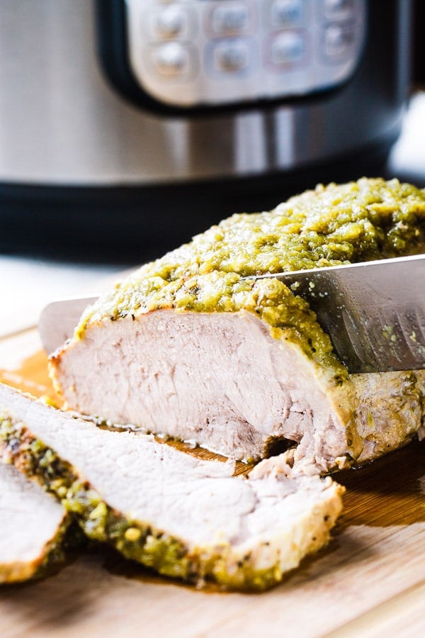 An Instant Pot salsa verde pork loin roast being sliced on a cutting board. 
