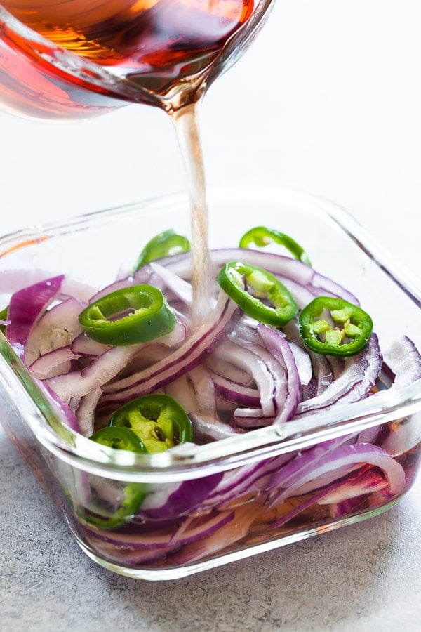 Pickling mixture being poured over jalapeños and red onions. 