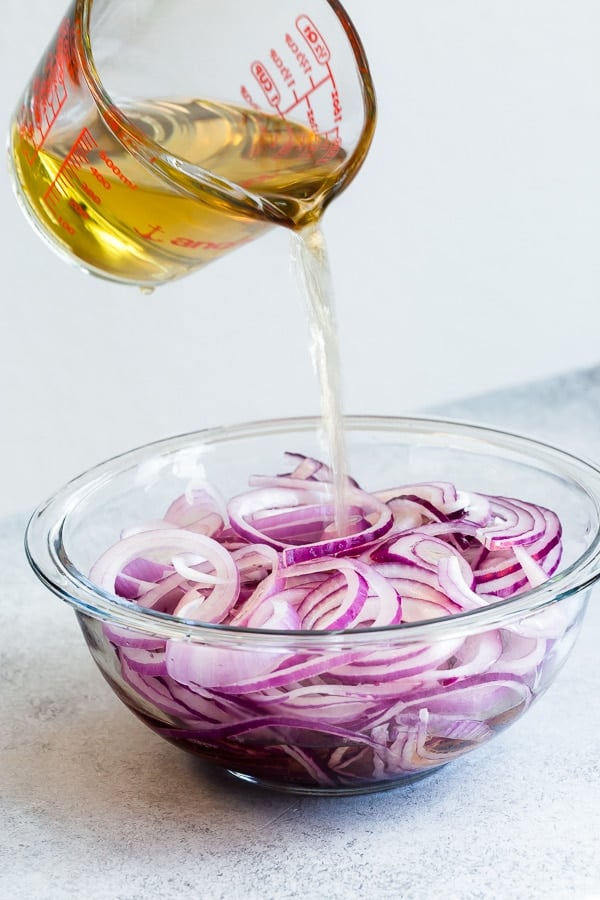 Pickling liquid being poured over a large bowl of sliced red onions. 