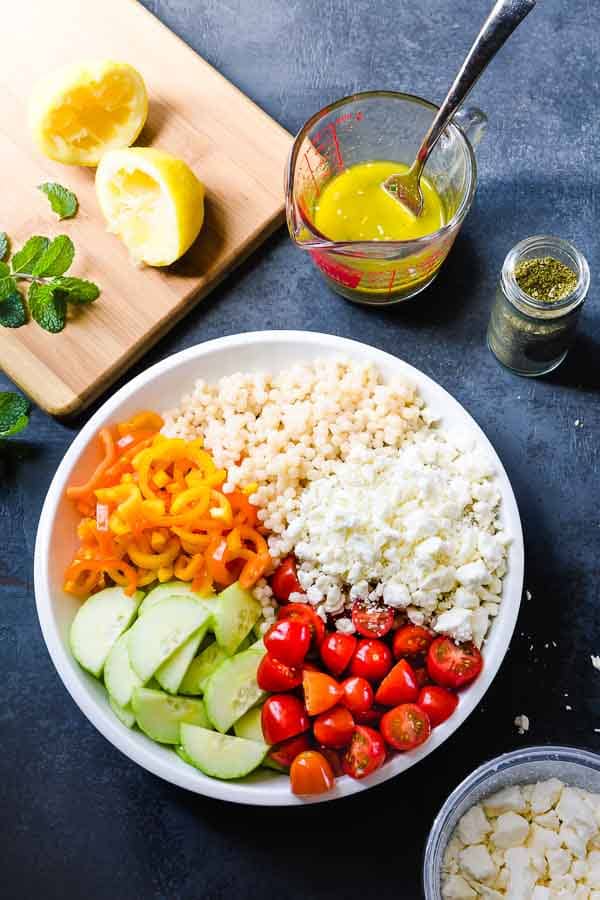 Overhead image of a bowl of couscous salad with a measuring cup of dressing.