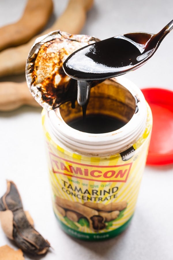 A spoon lifting a scoop of tamarind concentrate from a bottle.