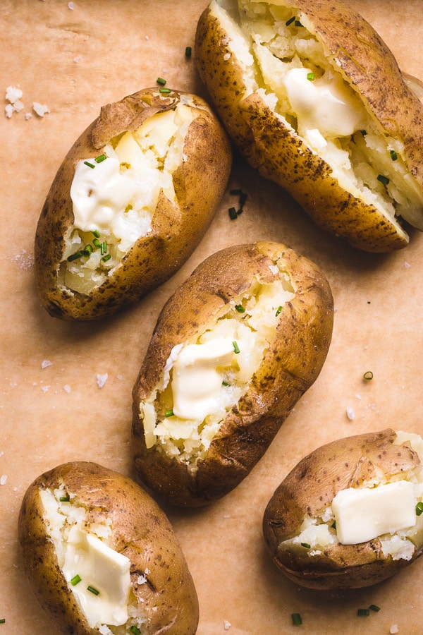 Baked potatoes arranged on a brown parchment paper and topped with a slice of butter and chives.