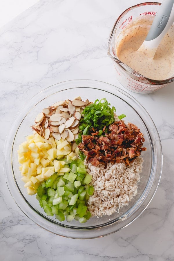 A bowl of turkey salad ingredients and a measuring cup of mayonnaise dressing. 