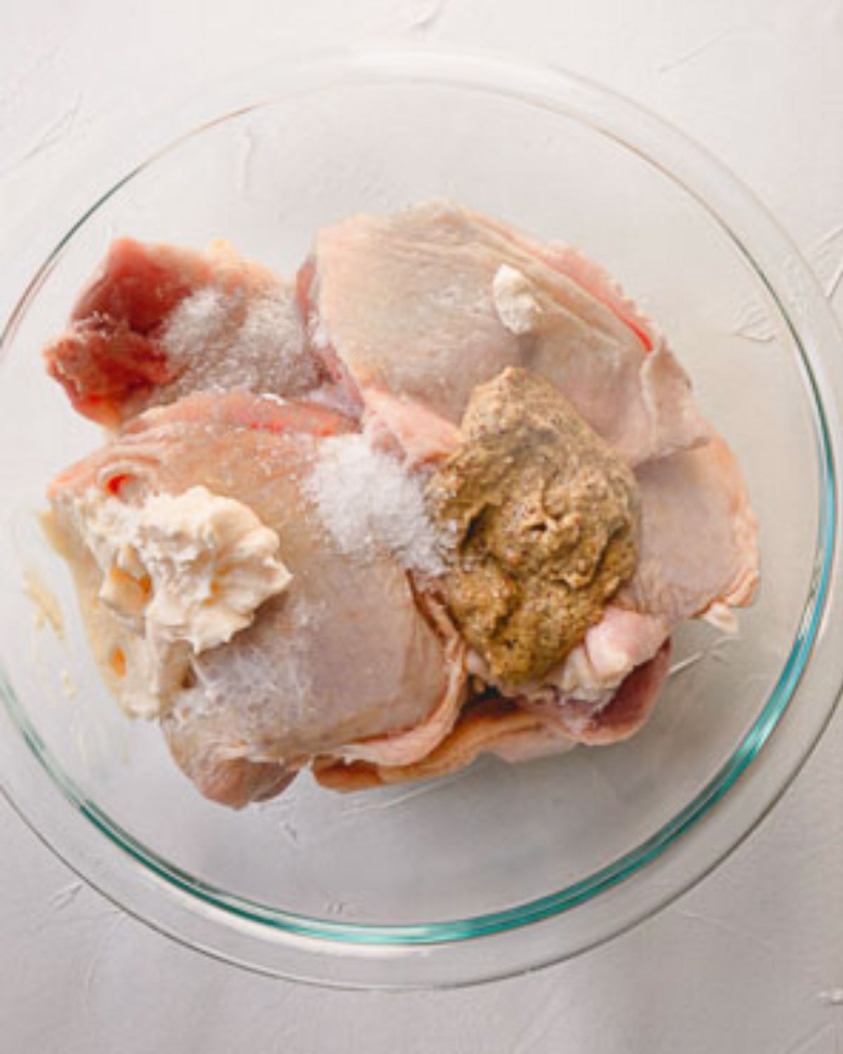 Chicken thighs, mayo, mustards, salt in a glass bowl.