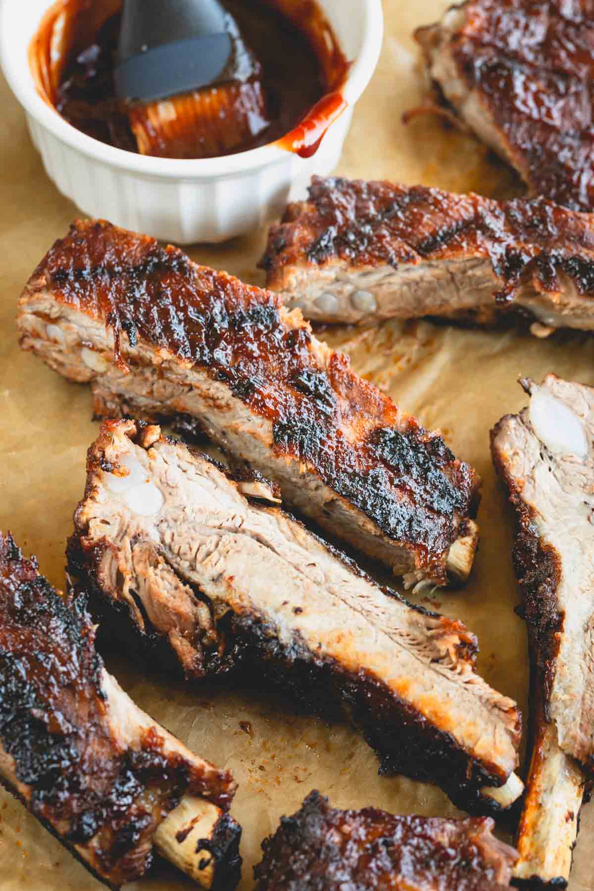 Cooked ribs on parchment paper next to a small bowl of BBQ sauce.