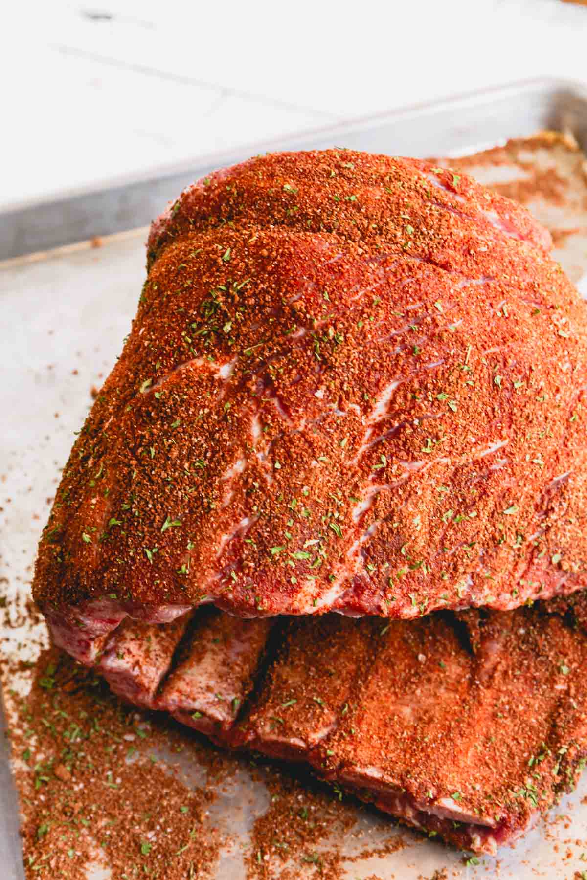 Ribs coated with the dry rub curled on a baking sheet.