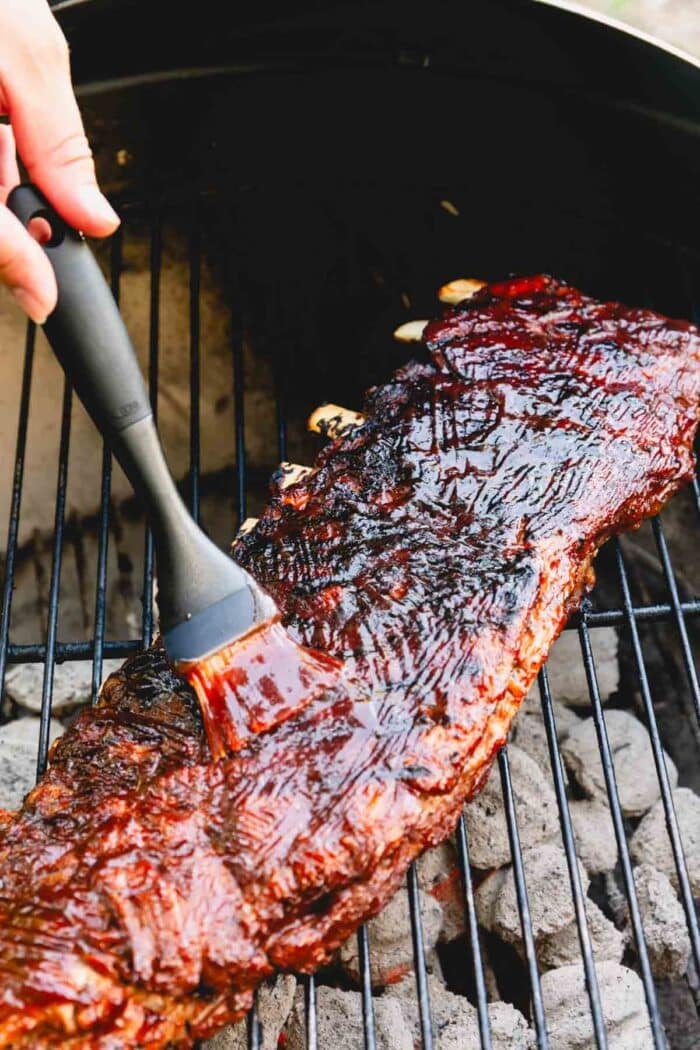 Ribs being cooked over a charcoal grill and brushed on with bbq sauce.