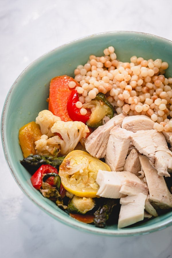 A blue bowl with roasted vegetables, couscous, and chicken.