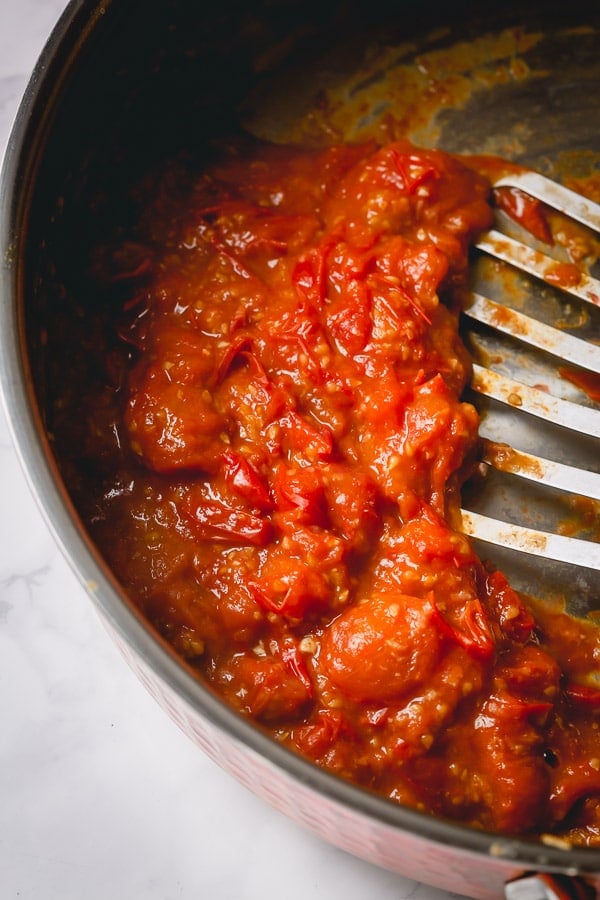A spatula in a pot of cherry tomato sauce. 