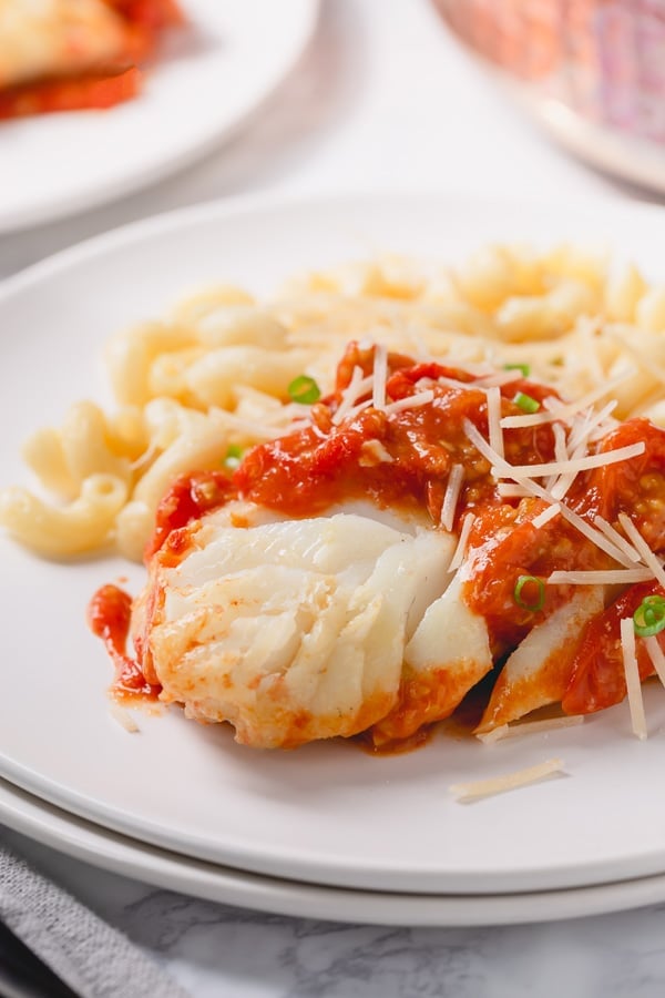 Close up image of pan-seared cod topped with tomato sauce on a plate with pasta. 