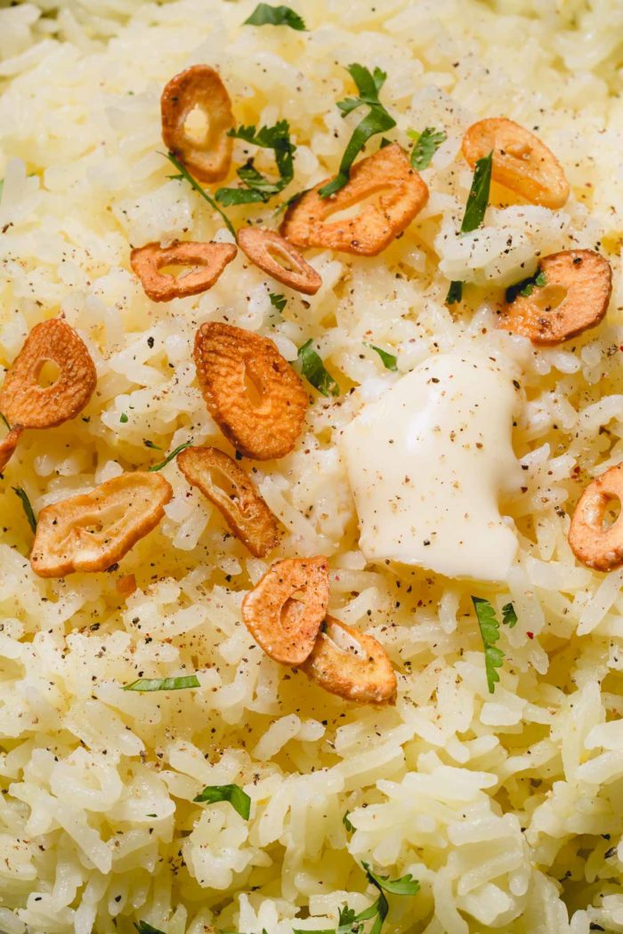 Upclose shot of rice topped with garlic chips, slice of butter and fresh herbs.