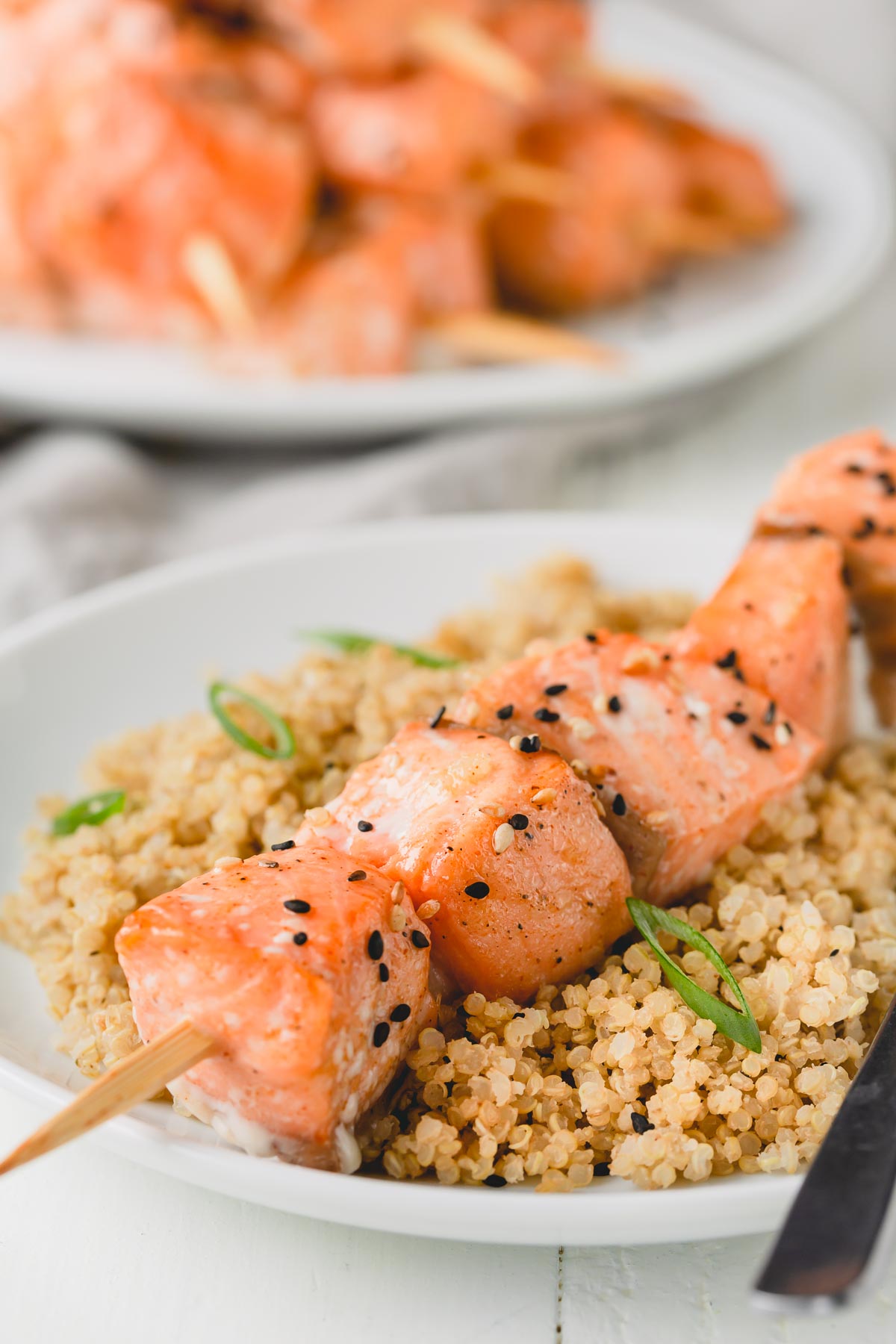 a salmon skewer over a bed of quinoa on a white plate.