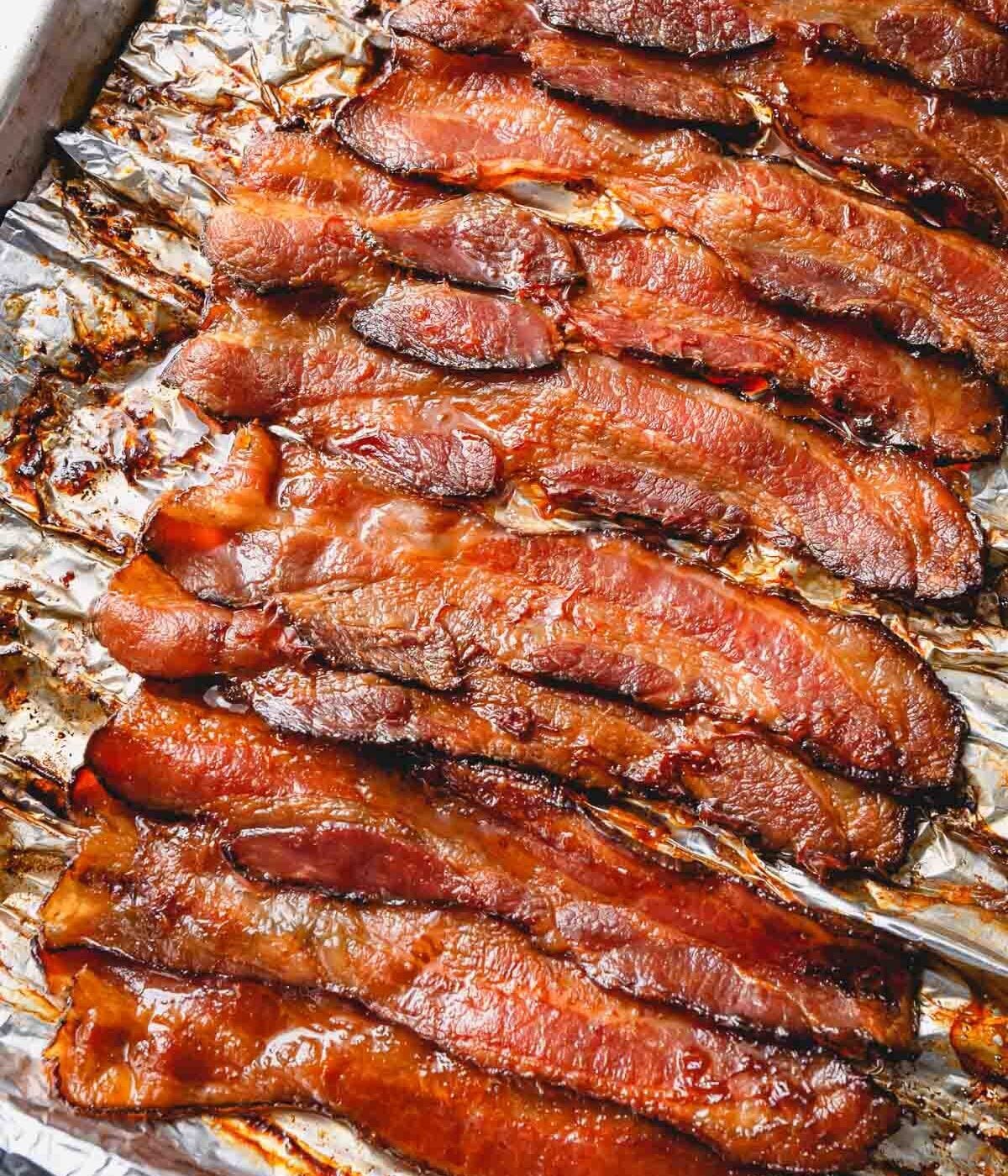 Cooked bacon strips on a baking sheet lined with a foil.