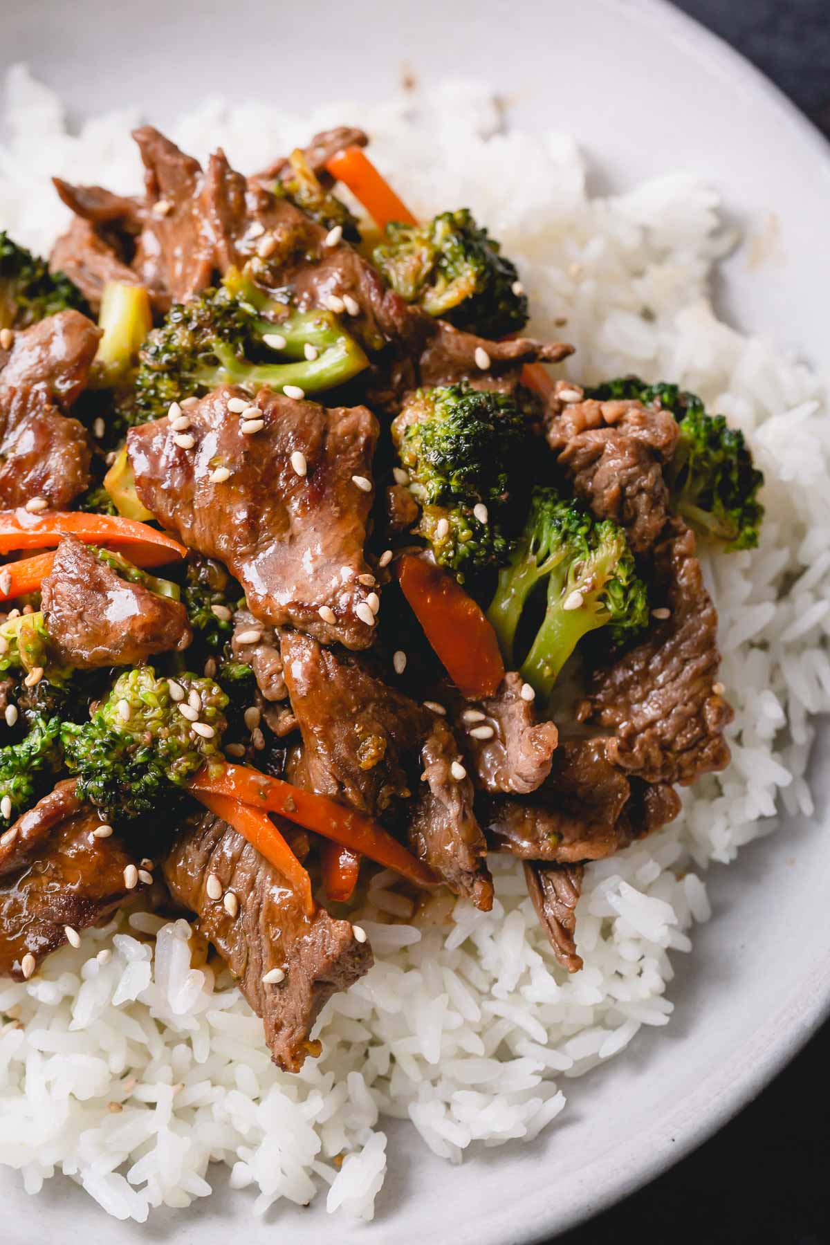Beef and broccoli stir fry on a white plate with carrots, broccoli, and white rice.