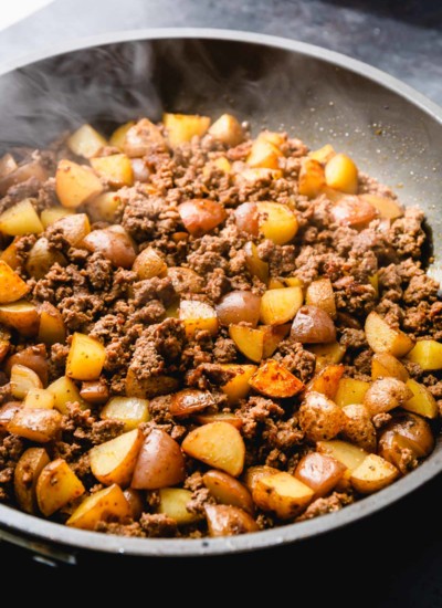 Ground beef potato hash cooking in a large black skillet.
