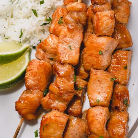 Chicken skewers on white plate with rice and lime as a garnish.