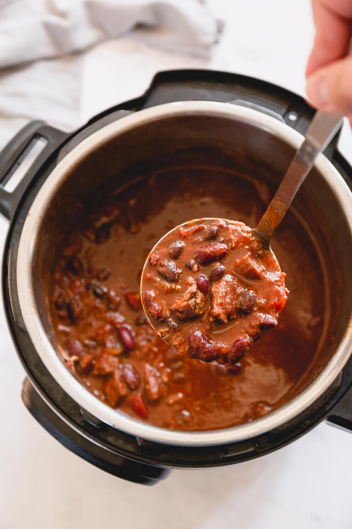 A ladle of chunky chili over Instant Pot of chili.