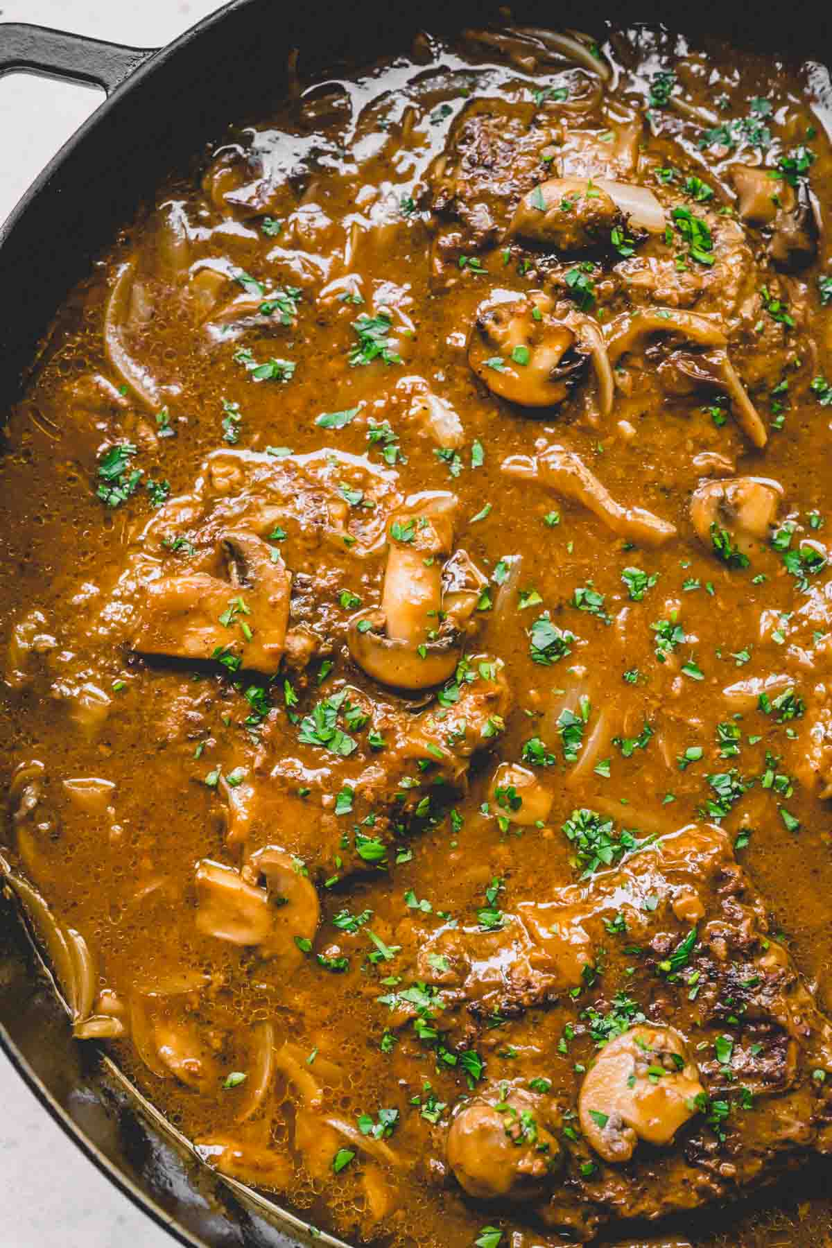 Smothered steak with mushroom gravy in a skillet.