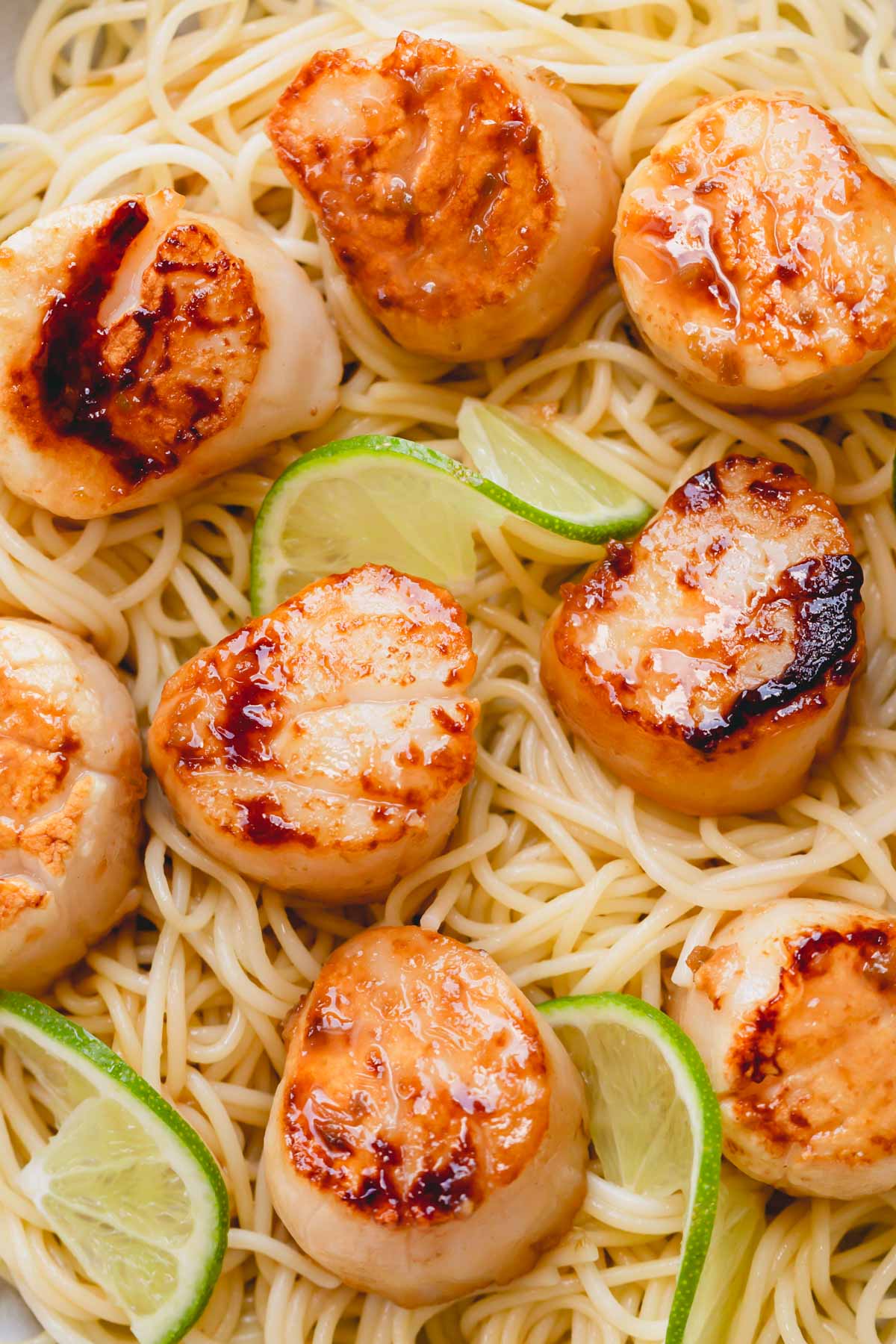 Seared scallops over noodles garnished with lime slices.