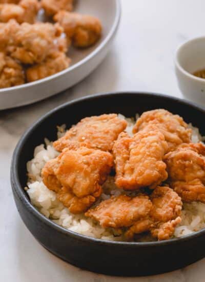 Mochiko chicken over a bed of white rice in a dark shallow bowl.
