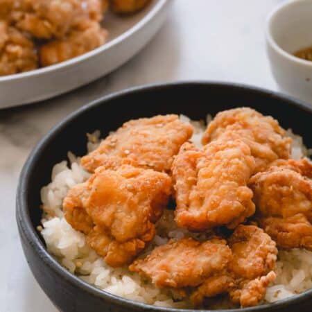 Mochiko chicken over a bed of white rice in a dark shallow bowl.