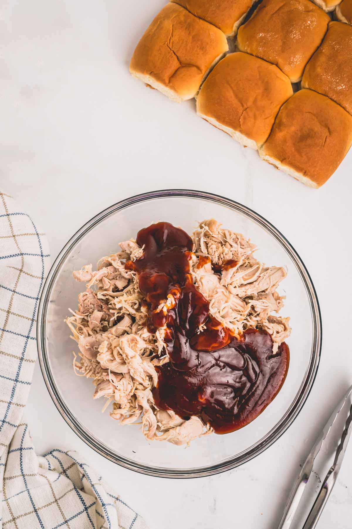 Shredded chicken in a glass bowl topped with bbq sauce.
