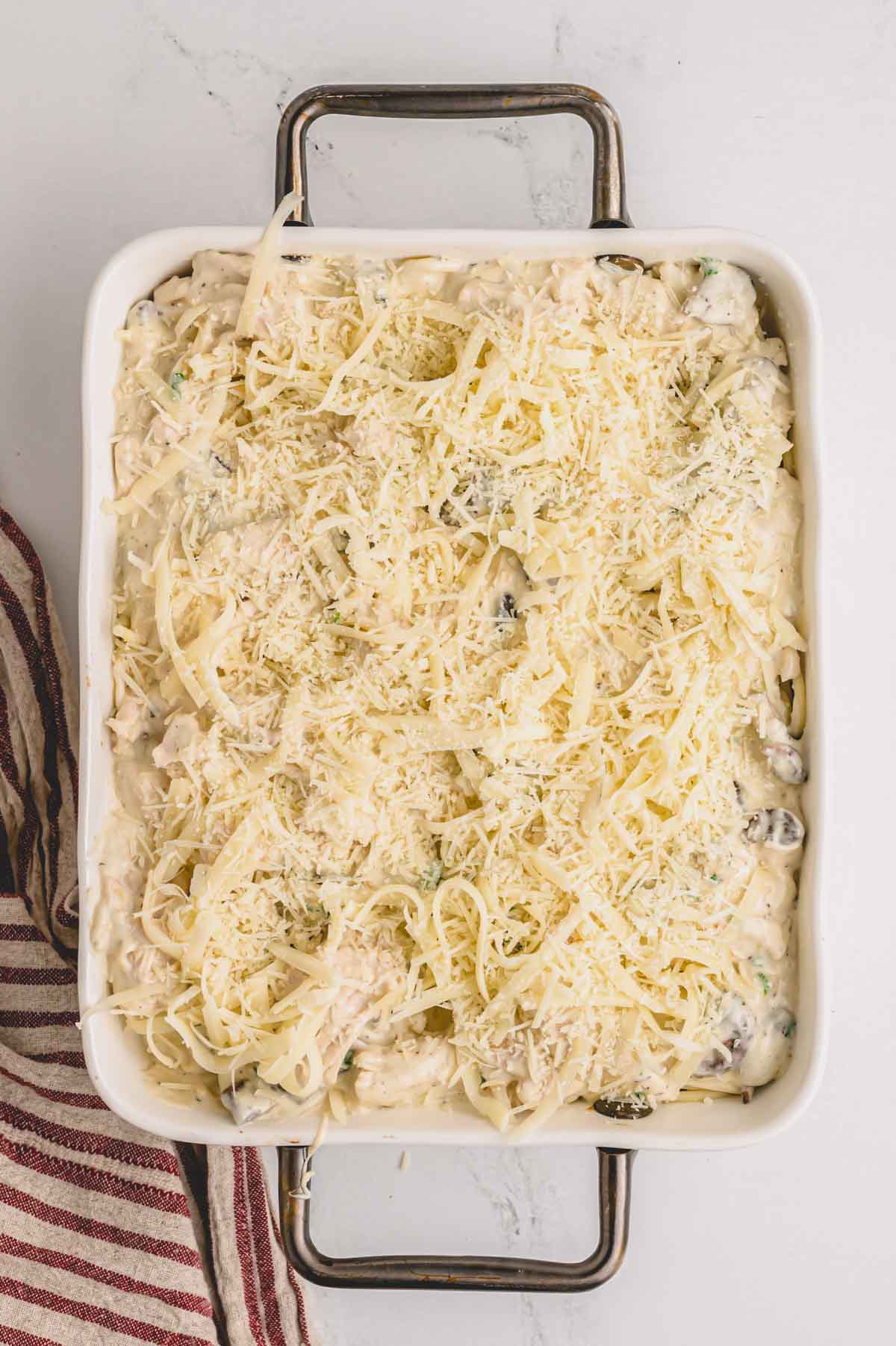 Uncooked tetrazzini sprinkled with cheese in a baking dish.